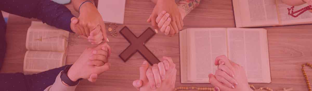 Youth having devotion over a wooden cross with the bible on a table.